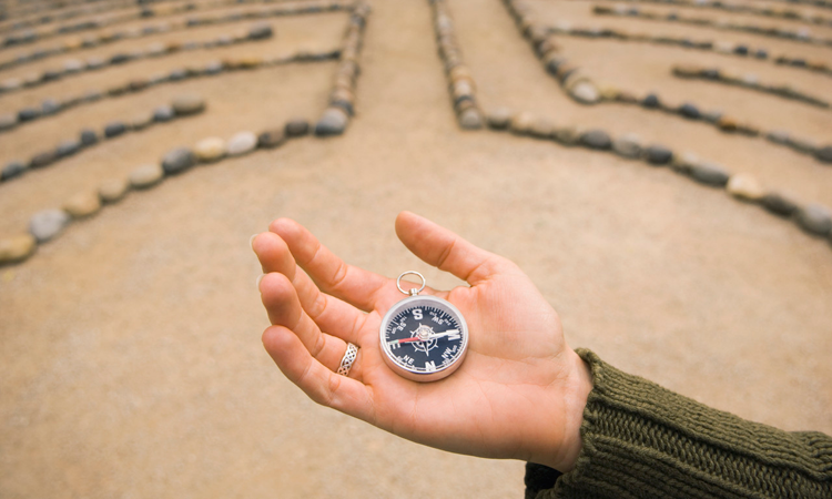 Woman's hand holding compass, labyrinth background