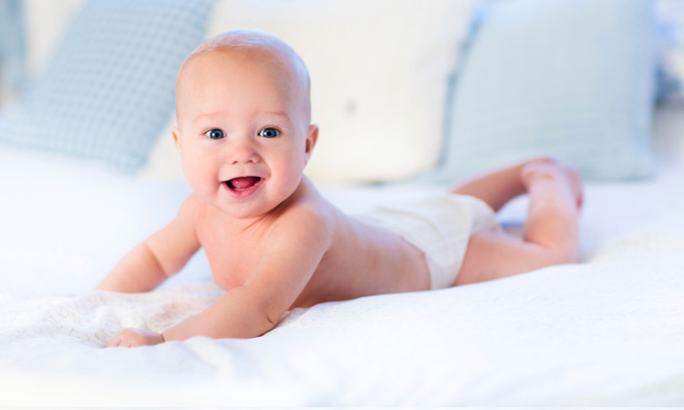 baby with diapers smiling on bed