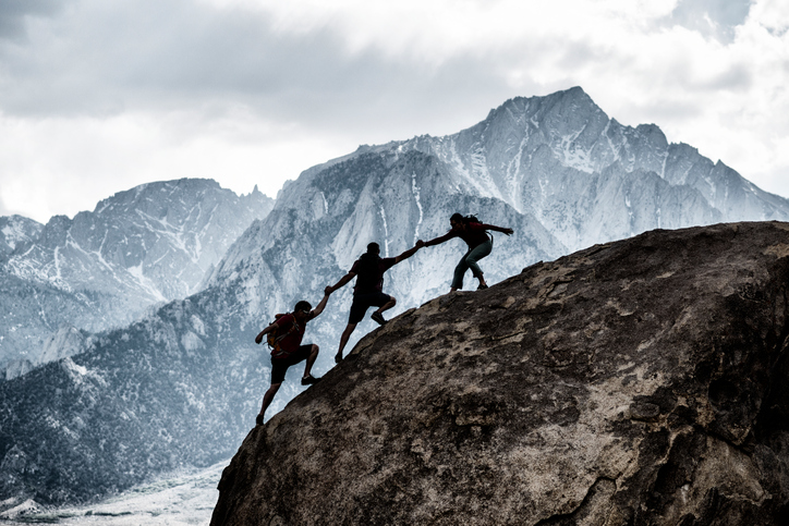 three friends climbing mountain achieving goals