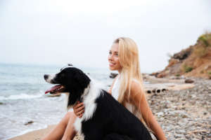 Smiling woman with dog sitting on the beach and thinking