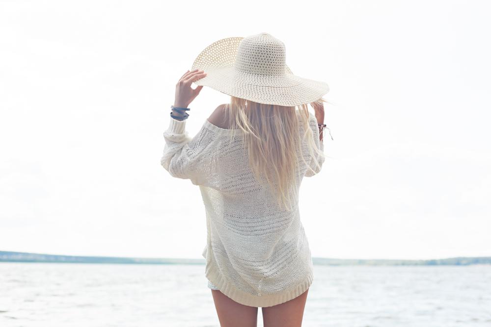 Young woman in hat and white pullover having rest by the sea living in abundance